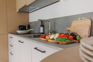 A modern kitchen with a stainless steel sink, a wooden cutting board with vegetables, and a wine bottle. - Sea Breeze by Grandeur Property (Poole)