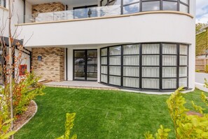 A modern two-story house with a curved glass facade, a brick section, and a well-maintained lawn. - Sea Breeze by Grandeur Property (Poole)