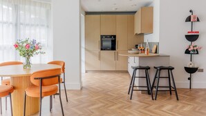 Una cucina moderna con mobili in legno, forno integrato e zona pranzo con tavolo rotondo e sedie arancioni.