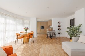A modern living room with a dining area, kitchen, and a large window with sheer curtains. - Sea Breeze by Grandeur Property (Poole)