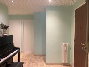 Ein Zimmer mit einem Klavier, einer Heizung und einer Tür.