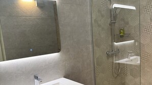 Ein Badezimmer mit weißem Waschbecken, einem Spiegel und einer Dusche mit Glastür.