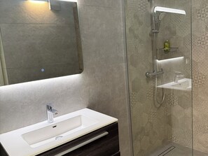 Ein Badezimmer mit weißem Waschbecken, einem Spiegel und einer Dusche mit Glastür.