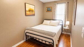 A bedroom with a bed, a nightstand, a window with curtains, and wall art.