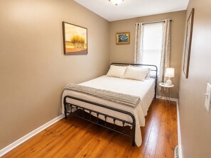 A bedroom with a bed, a nightstand, a window with curtains, and wall art.