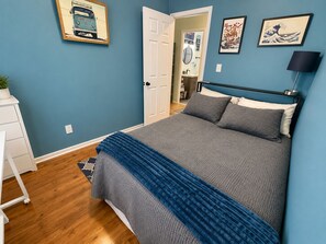 Een slaapkamer met een bed, een ladekast, een deur en twee kunstwerken aan de muur.