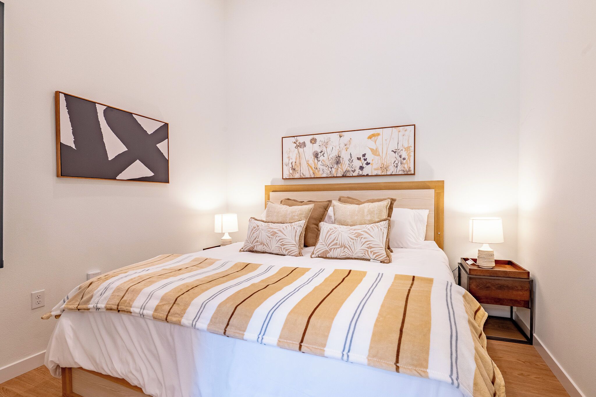 A neatly made bed with a striped bedspread, two bedside lamps, and a framed floral artwork above the bed.