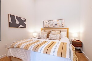 Una cama bien tendida con una colcha a rayas, dos lámparas de noche y una obra de arte floral enmarcada sobre la cama.