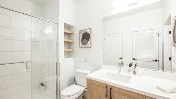 A modern bathroom with a glass shower enclosure, a white toilet, and a wooden vanity with a large mirror.