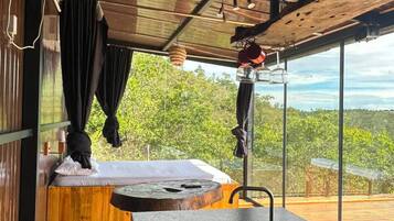 Habitación con piso de madera, un ventanal grande, cama, lavamanos y vistas al exterior.