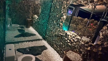 Un baño con un diseño único que incluye una pared de piedra, cabina de vidrio y un inodoro moderno.