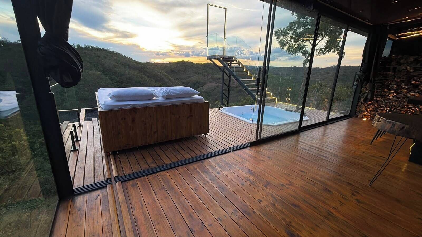 A bedroom with a wooden floor, a bed with pillows, a glass wall, and a hot tub.