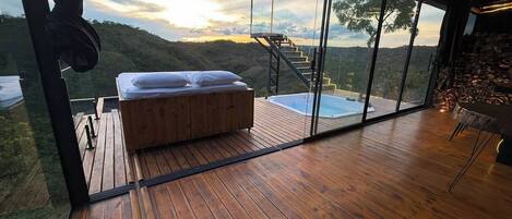 A bedroom with a wooden floor, a bed with pillows, a glass wall, and a hot tub.