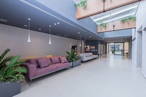 Eine moderne Lobby mit einer violetten Couch, einer grauen Couch und Topfpflanzen.