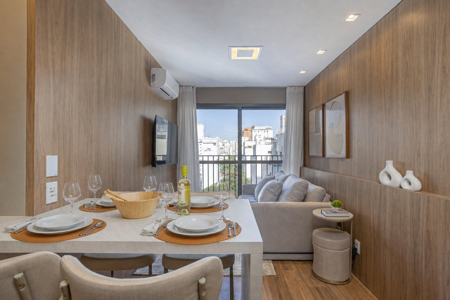 Uma área de refeições moderna com uma mesa posta para dois, um sofá e uma pequena mesinha lateral com objetos decorativos.