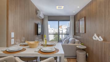Uma área de refeições moderna com uma mesa posta para dois, um sofá e uma pequena mesinha lateral com objetos decorativos.