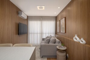 Ein modernes Wohnzimmer mit einer Couch, einem Flachbildfernseher und einem kleinen runden Tisch mit einem Buch.