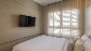 A hotel room with a bed, a flat-screen TV mounted on the wall, and a window with sheer curtains. - ON Augusta (São Paulo)