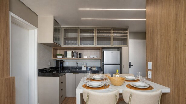 A modern kitchen with a dining area set for four, featuring a refrigerator, microwave, and coffee maker. - ON Augusta (São Paulo)