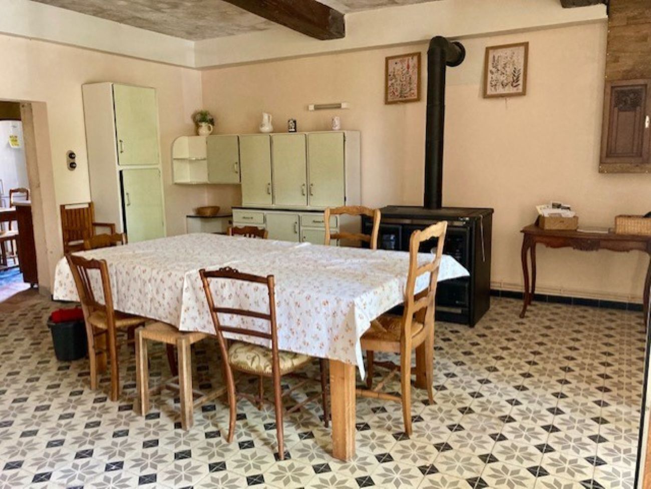Una zona de menjador amb una taula preparada per a quatre persones, envoltada de caires de fusta. Hi ha una cuina al fons amb armaris i una estufa.