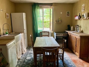 Cocina compacta con mesa, sillas, refrigerador, estufa y ventana con cortinas.