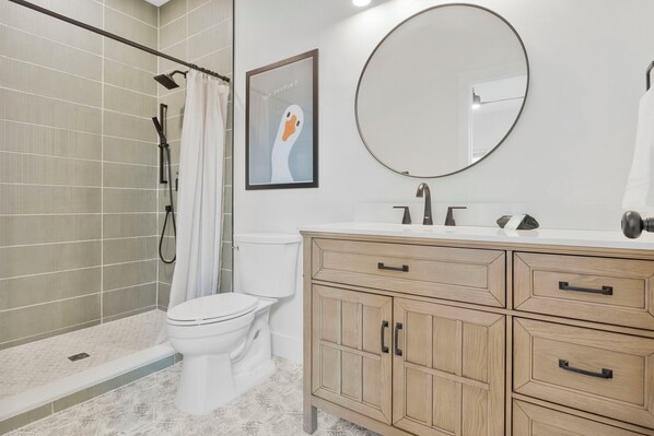 A bathroom with a shower, toilet, vanity with drawers, and a large mirror. - M Street Loft - One-of-a-Kind Pensacola Getaway (Pensacola)
