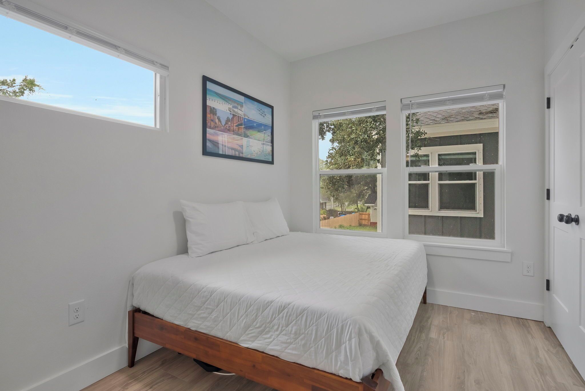 A bedroom with a bed, a window with a view, and a painting on the wall.