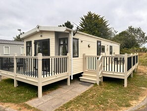 A mobile home with a porch and a deck, surrounded by grass and trees. - Homely Caravan in Skegness - Sleeps 6 (Skegness)