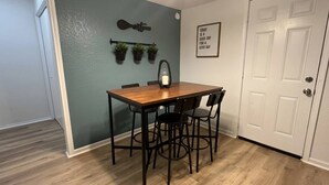 A dining area with a wooden table and four chairs, a wall-mounted light, and a door with a decorative plate. - Welcoming 2-bedroom house with AC in Arlington, near AT&T Stadium &Six Flags (Arlington)