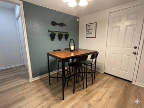 A dining area with a wooden table and four chairs, a wall-mounted light, and a door with a decorative plate. - Welcoming 2-bedroom house with AC in Arlington, near AT&T Stadium &Six Flags (Arlington)