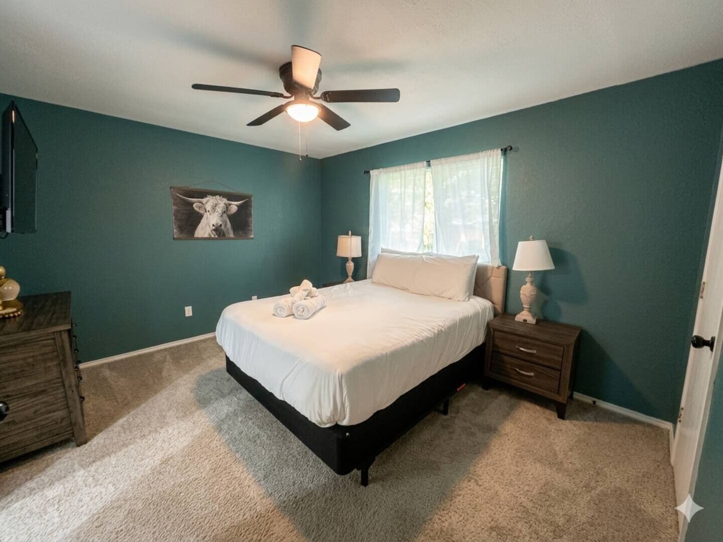 Une chambre à coucher comprenant un lit, des tables de chevet, un ventilateur de plafond et une lampe fixée au mur.