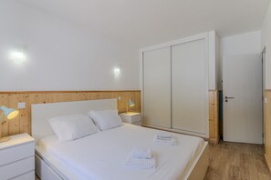 A hotel room with a bed, two bedside tables, a wooden headboard, a wardrobe, and a door. - #400 Central Albufeira Oasis | 1BR & Pool (Albufeira)