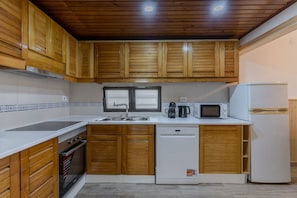 A compact kitchen with wooden cabinets, a built-in oven, a dishwasher, a microwave, and a sink. - #400 Central Albufeira Oasis | 1BR & Pool (Albufeira)