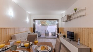 A modern interior with a dining area, a sofa, a TV, and a view through a glass door. - #400 Central Albufeira Oasis | 1BR & Pool (Albufeira)