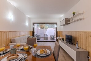 Um interior moderno com uma área de jantar, um sofá, uma TV e uma vista através de uma porta de vidro.