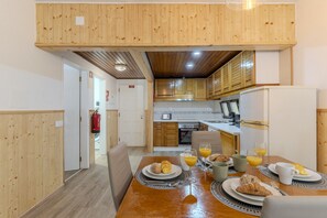 Uma cozinha moderna com armários de madeira, uma mesa de jantar posta para o café da manhã e um extintor de incêndio visível.