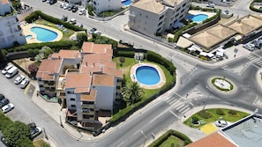 A multi-story hotel with a swimming pool, a roundabout, and a parking area. - #400 Central Albufeira Oasis | 1BR & Pool (Albufeira)