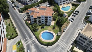 A multi-story building with a swimming pool, parking area, and surrounding greenery. - #400 Central Albufeira Oasis | 1BR & Pool (Albufeira)