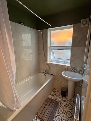 A bathroom with a bathtub, a window with a view, a sink, and a shower. - Apartment Sleeps 4 With Parking (London)