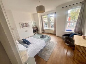 A modern bedroom with a bed, bedside table, chair, and a view of the street through a window. - Apartment Sleeps 4 With Parking (London)