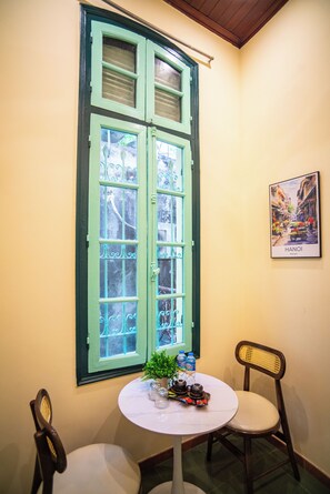 A room with a large window, a small round table with a plant and water bottles, two chairs, and a framed picture on the wall.