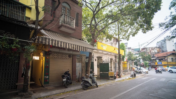 Vista de la calle con edificios, una moto estacionada y un letrero amarillo.