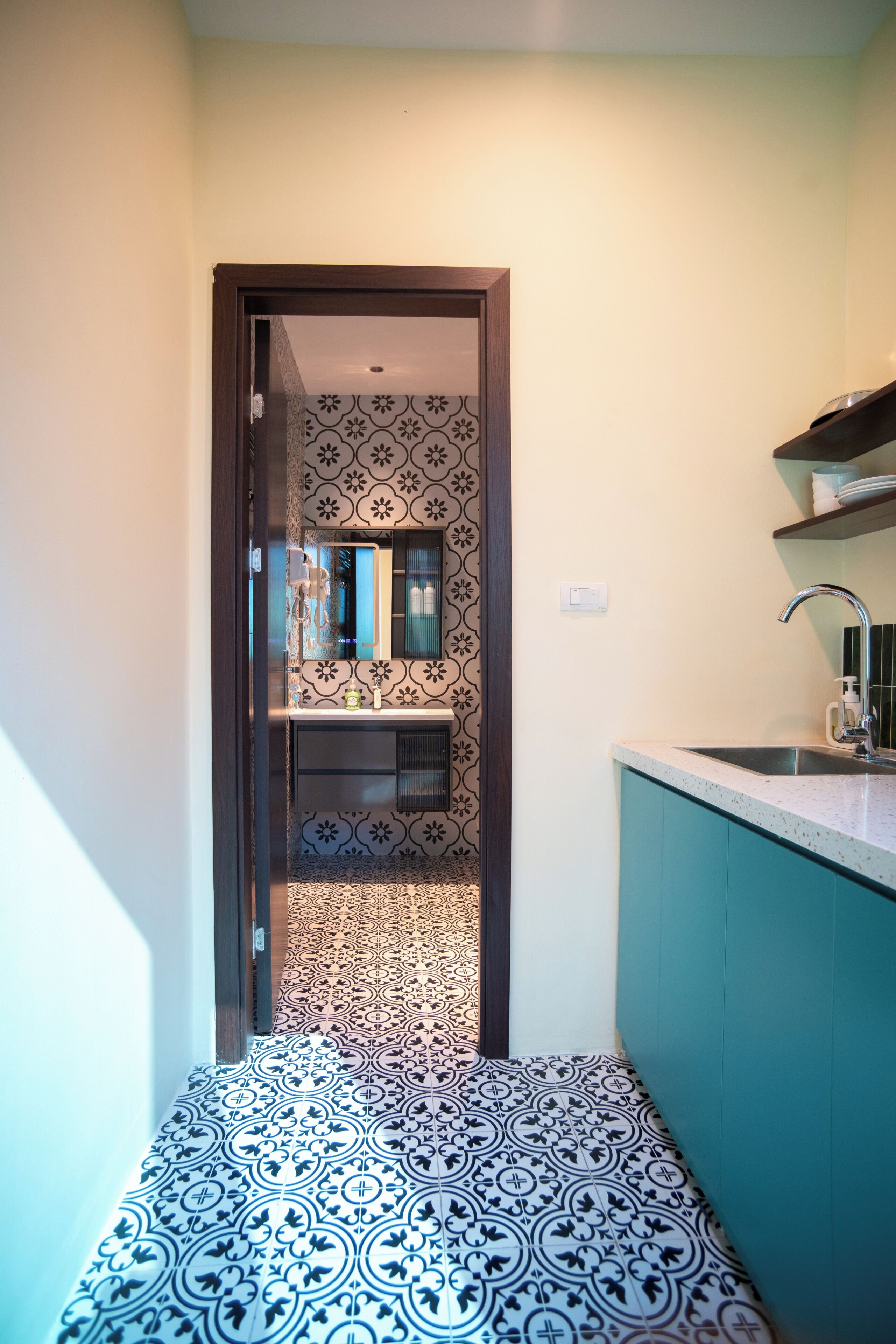 Un pasillo estrecho con baldosas de diseño que lleva a una zona de cocina con un lavamanos y armarios.