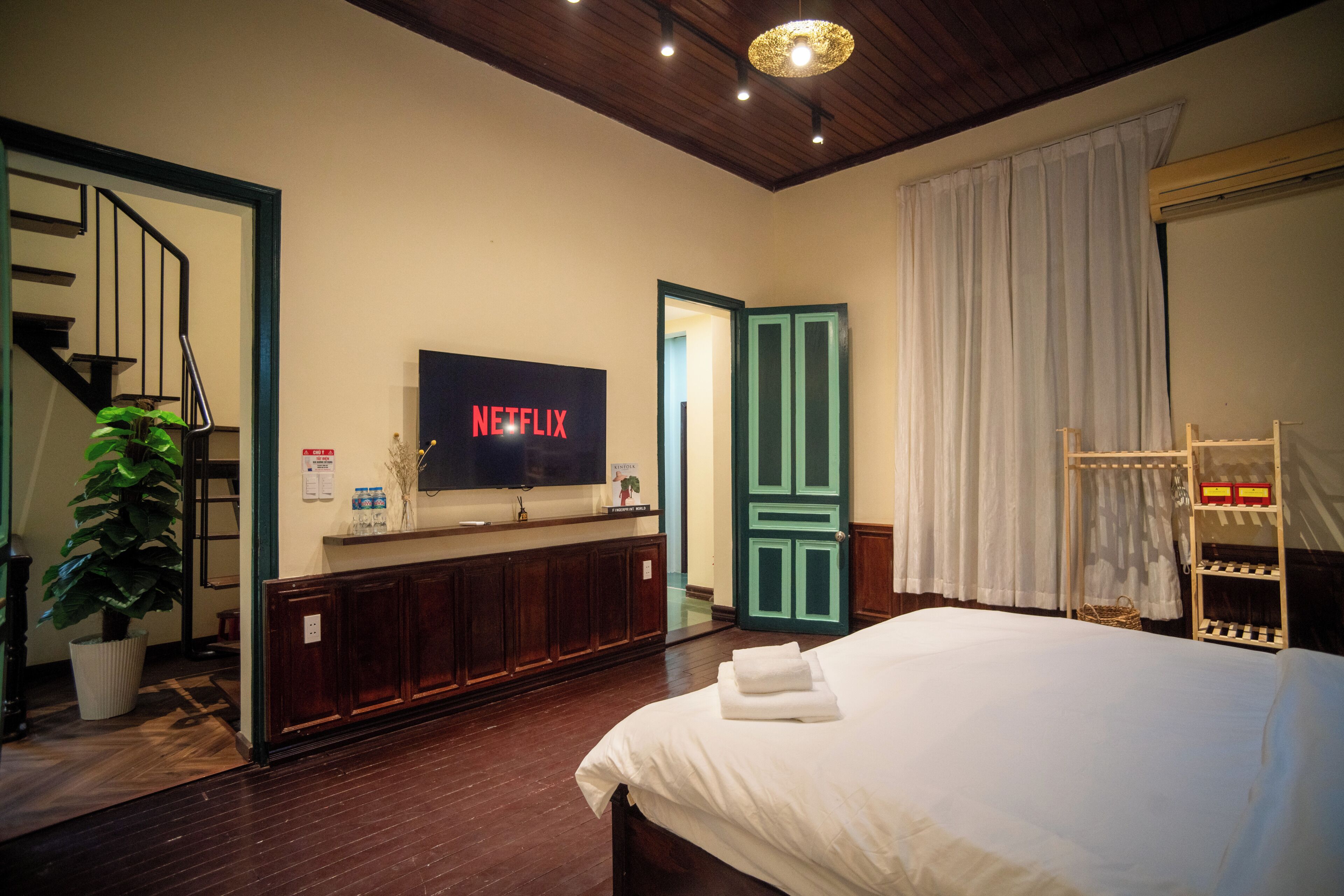 A hotel room with a bed, a television mounted on the wall, a wooden floor, a staircase, and a door.