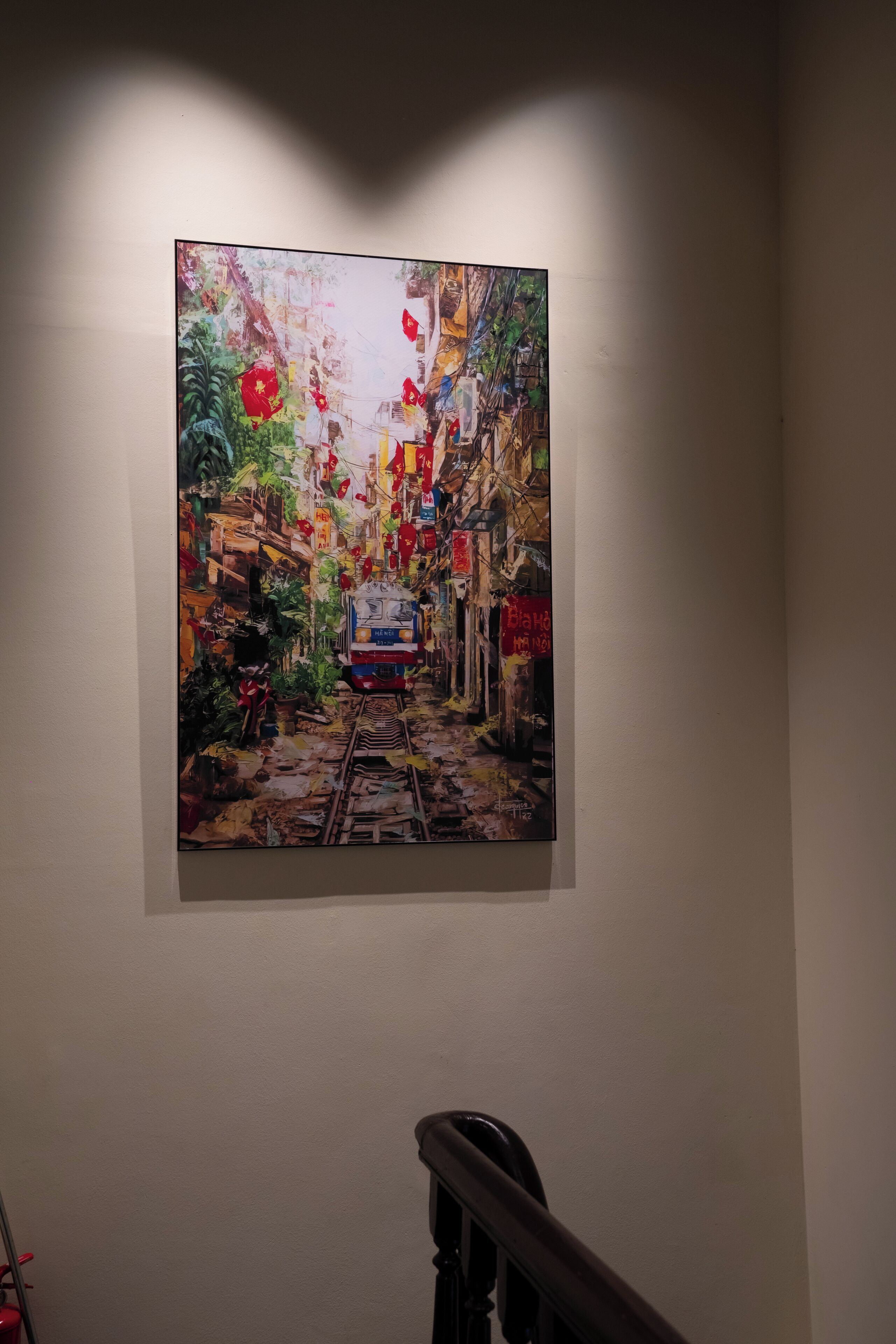 A painting of a narrow street with a train, hanging on a plain wall.