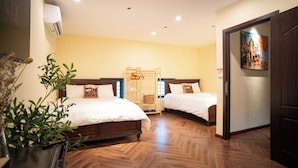 Habitación de hotel con dos camas, piso de madera, un cuadro en la pared y una planta en la esquina.