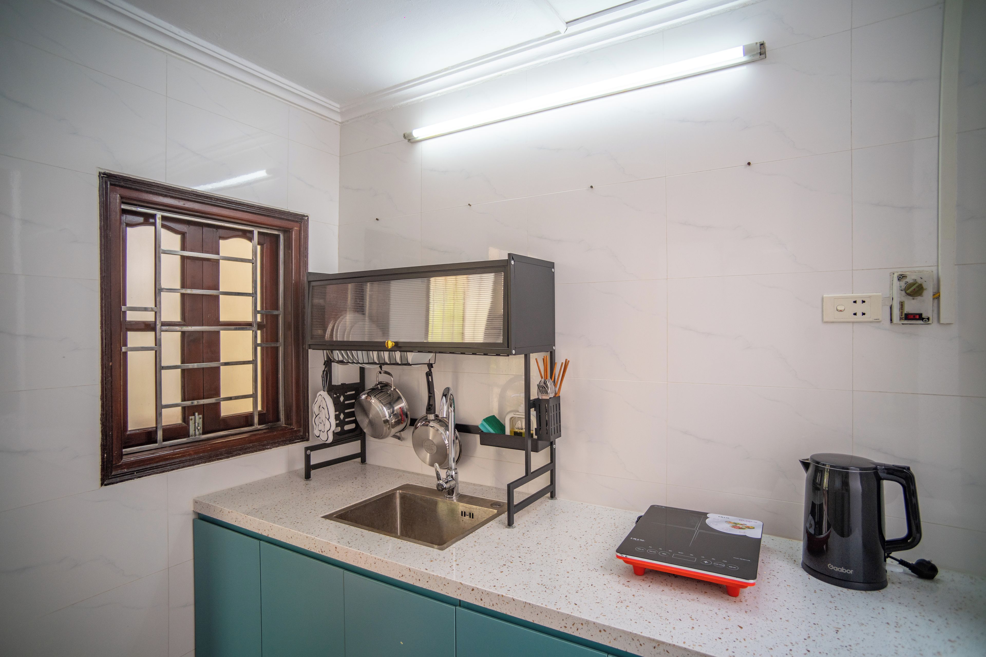 A kitchen with a stainless steel sink, a black range hood, a kettle, and a coffee maker.