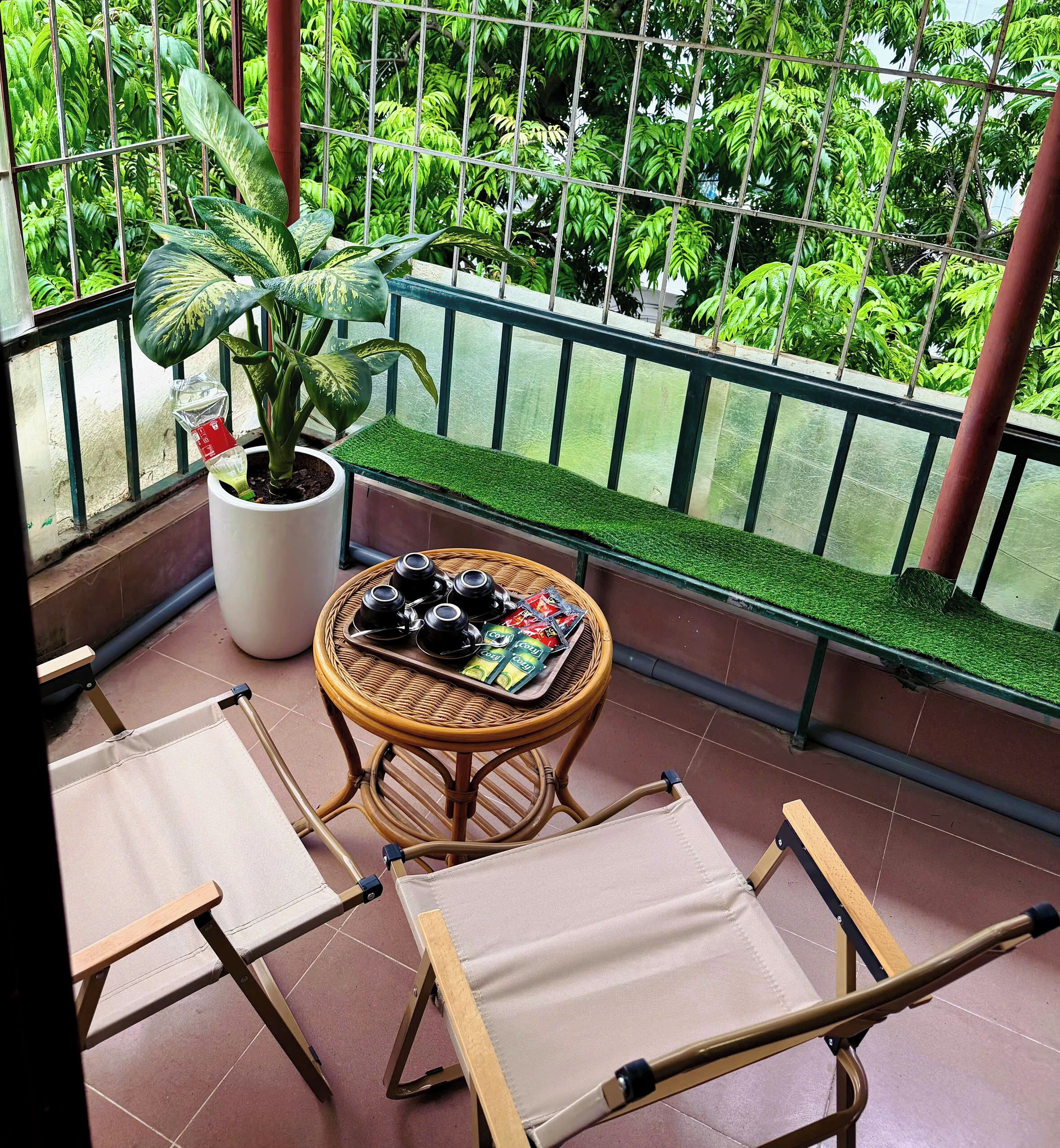 A balcony with a potted plant, a wicker table with tea sets, and two foldable chairs.