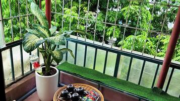 A balcony with a potted plant, a wicker table with tea sets, and two foldable chairs.