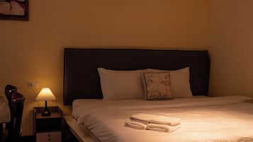 A hotel room with a bed, a nightstand with a lamp, an air conditioning unit, and a wall-mounted artwork.